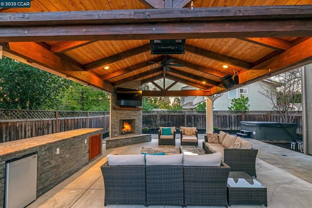 view of patio with ceiling fan, a gazebo, a hot tub, and an outdoor living space with a fireplace