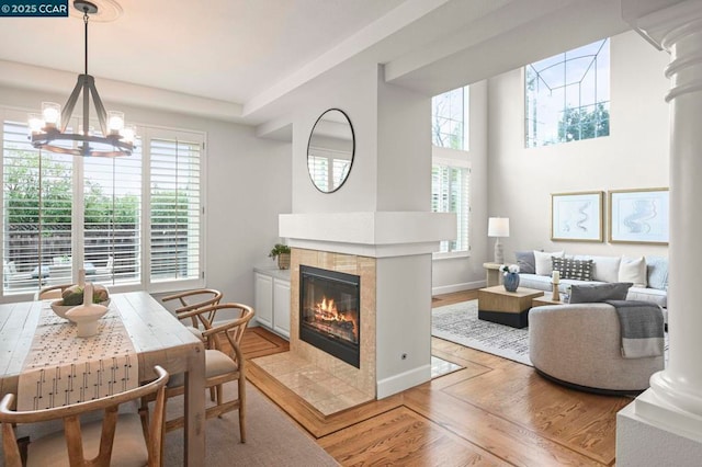 interior space featuring decorative columns, a notable chandelier, a tiled fireplace, light hardwood / wood-style floors, and a high ceiling