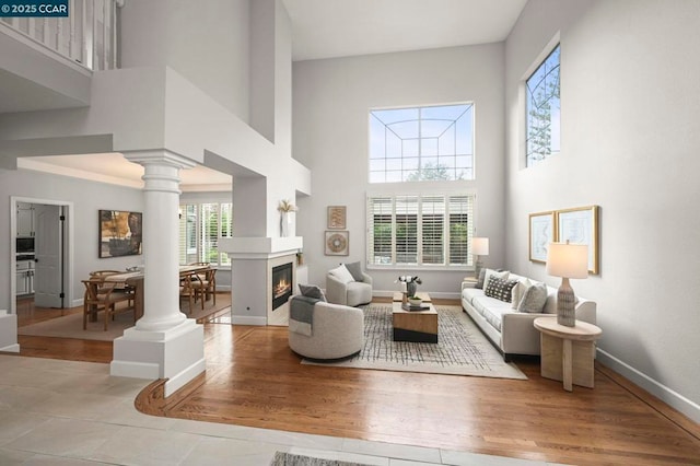 living room with decorative columns, a high ceiling, and light wood-type flooring