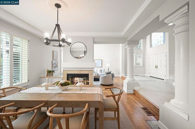 dining area featuring decorative columns, wood-type flooring, a tiled fireplace, and a notable chandelier