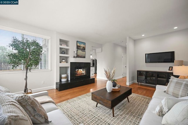 living room featuring wood-type flooring, a multi sided fireplace, and built in features