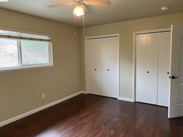 unfurnished bedroom with multiple closets, ceiling fan, and dark hardwood / wood-style flooring