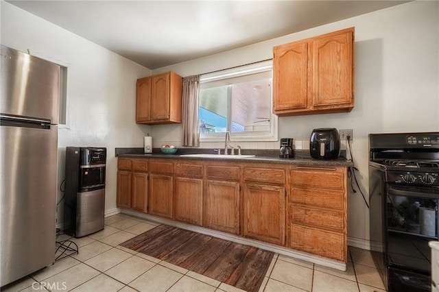 kitchen with sink, light tile patterned floors, stainless steel refrigerator, and black gas stove