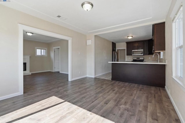 kitchen with dark brown cabinetry, sink, wood-type flooring, appliances with stainless steel finishes, and kitchen peninsula