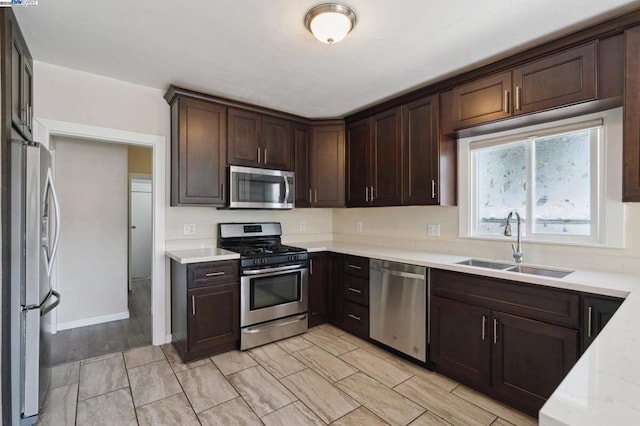 kitchen featuring stainless steel appliances, light stone countertops, sink, and dark brown cabinets