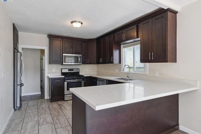 kitchen featuring appliances with stainless steel finishes, sink, dark brown cabinetry, and kitchen peninsula