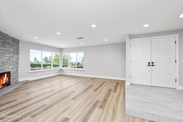 unfurnished living room featuring a stone fireplace and light wood-type flooring