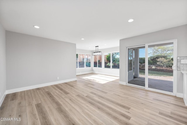 unfurnished living room featuring a notable chandelier and light wood-type flooring