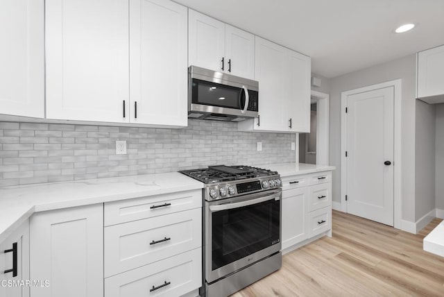 kitchen featuring tasteful backsplash, light hardwood / wood-style flooring, appliances with stainless steel finishes, light stone countertops, and white cabinets