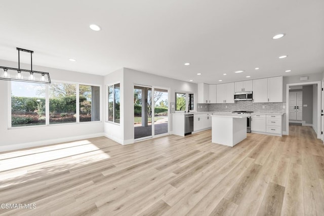 kitchen featuring white cabinetry, decorative light fixtures, appliances with stainless steel finishes, light hardwood / wood-style floors, and decorative backsplash