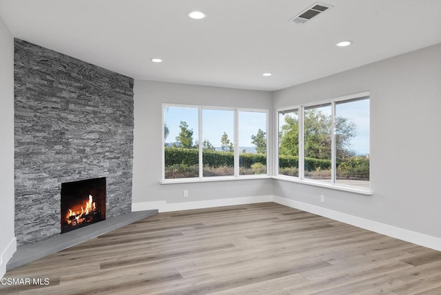 unfurnished living room with a stone fireplace and light wood-type flooring