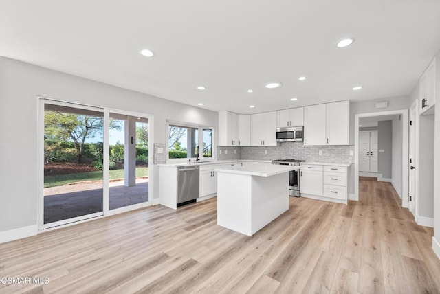 kitchen with appliances with stainless steel finishes, white cabinets, decorative backsplash, a center island, and light hardwood / wood-style floors