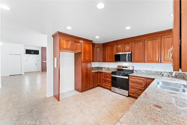 kitchen with light stone countertops, stainless steel appliances, a sink, and brown cabinetry