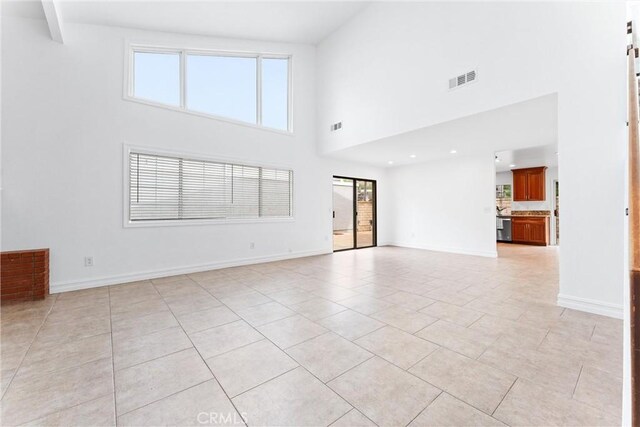 unfurnished living room with beamed ceiling, a towering ceiling, and light tile patterned floors