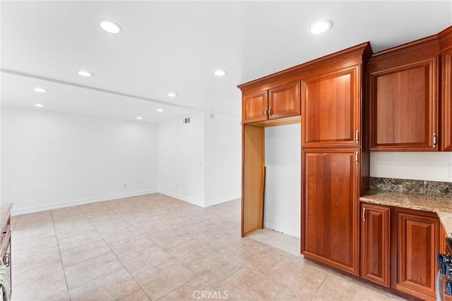 kitchen featuring light stone countertops, baseboards, brown cabinets, and recessed lighting