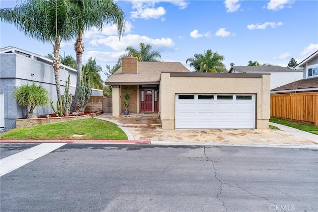 view of front of house featuring a chimney, stucco siding, an attached garage, fence, and driveway