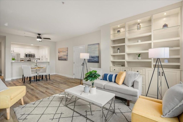 living room with ceiling fan, built in features, and light wood-type flooring