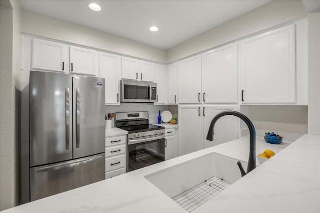 kitchen with white cabinetry, sink, stainless steel appliances, and light stone countertops