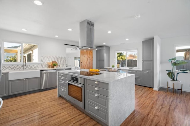 kitchen featuring sink, gray cabinetry, stainless steel appliances, a center island, and island range hood