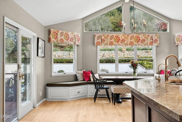 dining space featuring sink, a notable chandelier, light hardwood / wood-style floors, breakfast area, and vaulted ceiling