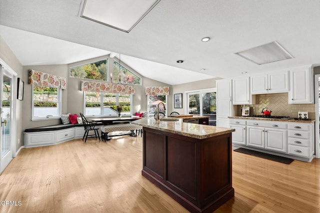 kitchen featuring vaulted ceiling, white cabinets, backsplash, light stone counters, and light hardwood / wood-style flooring