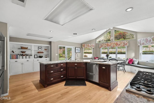 kitchen featuring dark brown cabinetry, sink, a kitchen island with sink, and light stone countertops