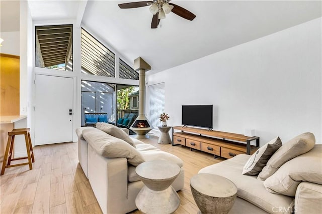 living room with ceiling fan, high vaulted ceiling, light wood-type flooring, and a wood stove