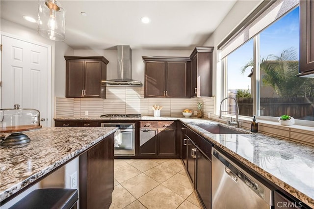 kitchen featuring sink, light stone counters, decorative light fixtures, appliances with stainless steel finishes, and wall chimney range hood