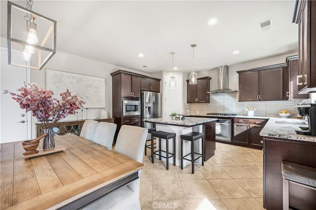 kitchen featuring hanging light fixtures, stainless steel appliances, a kitchen breakfast bar, a kitchen island, and wall chimney exhaust hood