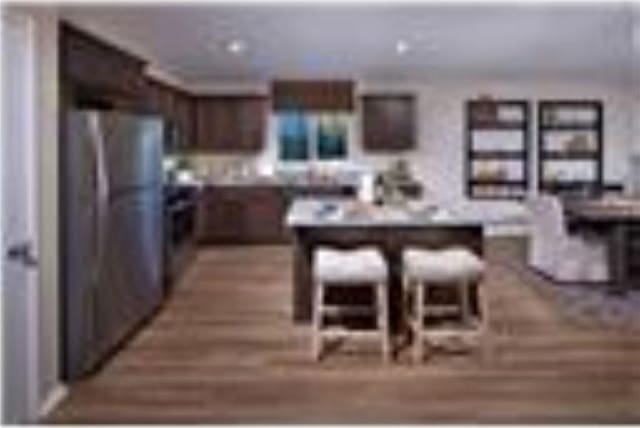 kitchen featuring dark brown cabinets, light hardwood / wood-style floors, stainless steel refrigerator, and a breakfast bar