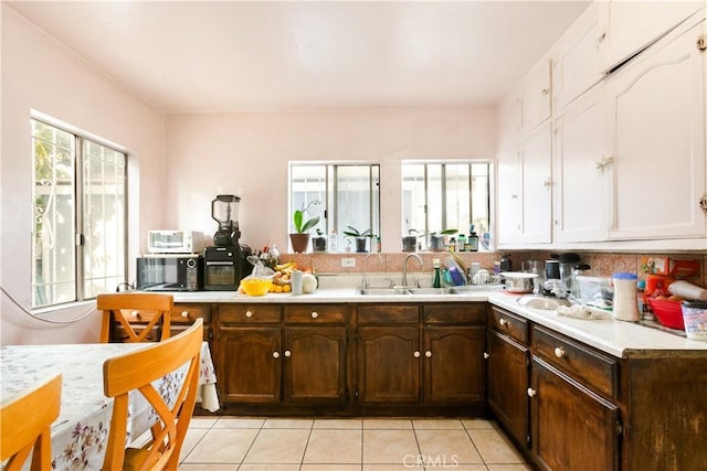 kitchen with dark brown cabinetry, light tile patterned floors, white cabinetry, and sink