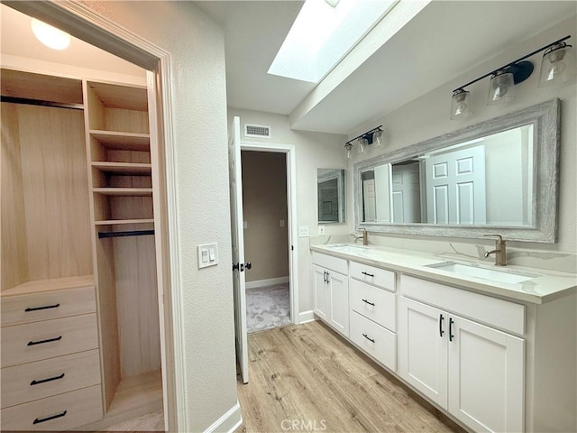 bathroom with double vanity, a skylight, visible vents, wood finished floors, and a sink