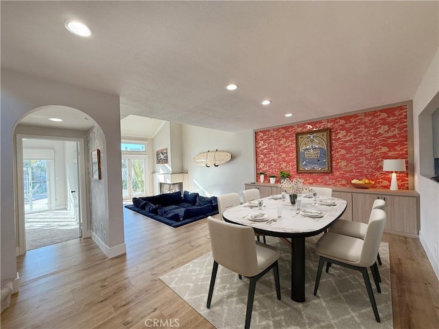 dining space with wallpapered walls, light wood finished floors, arched walkways, an accent wall, and recessed lighting