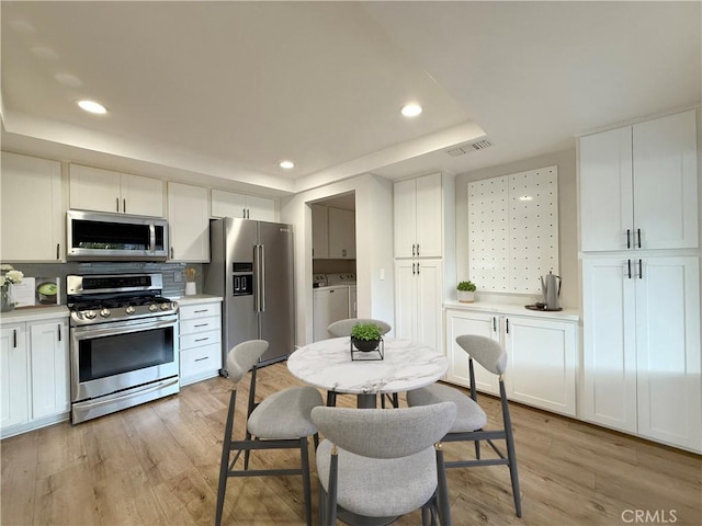 kitchen with light hardwood / wood-style flooring, white cabinetry, backsplash, stainless steel appliances, and independent washer and dryer