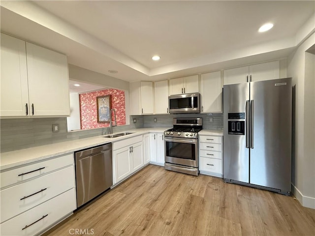 kitchen featuring light wood-style flooring, appliances with stainless steel finishes, light countertops, white cabinetry, and a sink