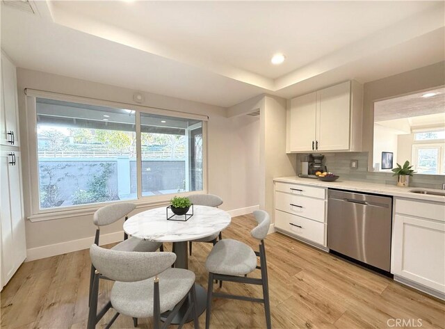 kitchen with light hardwood / wood-style flooring, white cabinets, dishwasher, a wealth of natural light, and backsplash