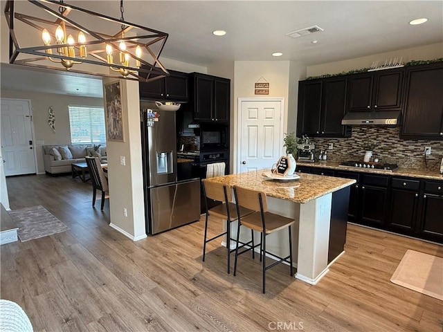 kitchen featuring a breakfast bar, decorative light fixtures, a center island, light stone countertops, and black appliances