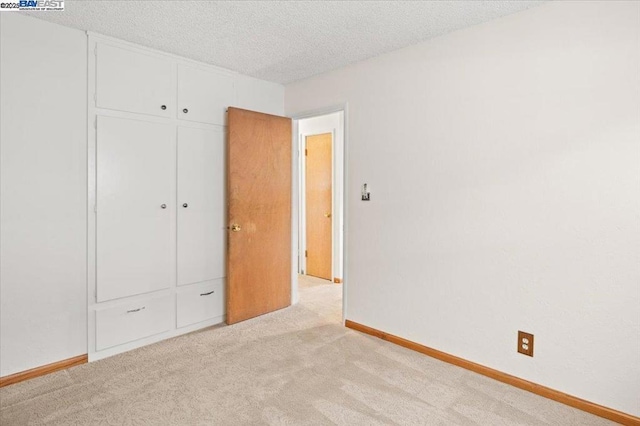 unfurnished bedroom with light colored carpet, a closet, and a textured ceiling