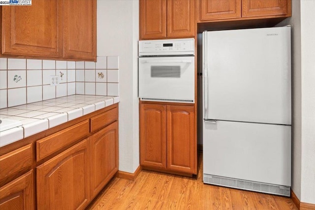 kitchen featuring tasteful backsplash, white appliances, tile counters, and light wood-type flooring