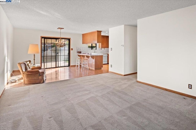 unfurnished living room with an inviting chandelier, light carpet, and a textured ceiling