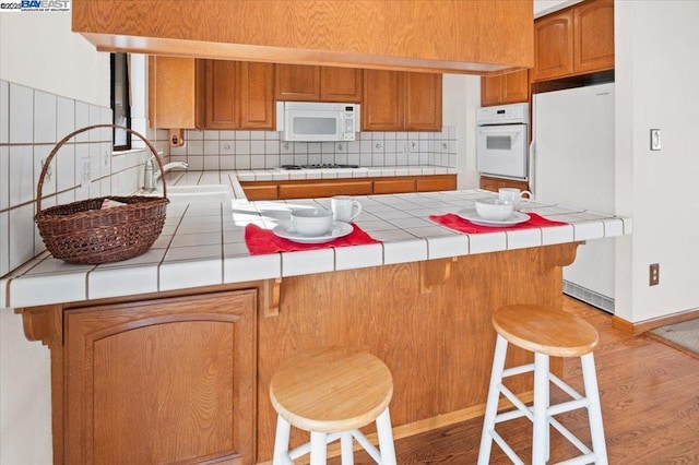 kitchen featuring a breakfast bar, tile counters, white appliances, and kitchen peninsula