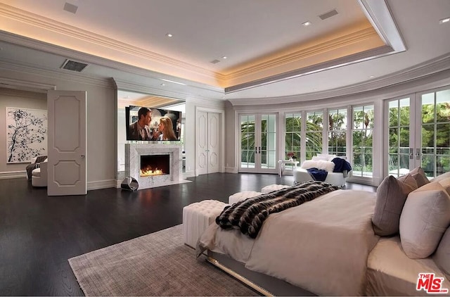 bedroom featuring dark hardwood / wood-style floors, a tray ceiling, a high end fireplace, ornamental molding, and french doors