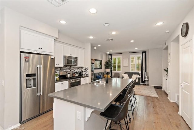 kitchen with sink, appliances with stainless steel finishes, white cabinetry, an island with sink, and a kitchen bar