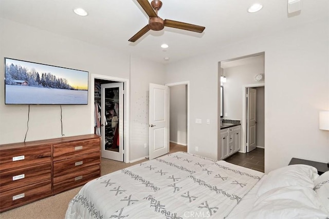 bedroom featuring ceiling fan, a spacious closet, connected bathroom, dark carpet, and a closet