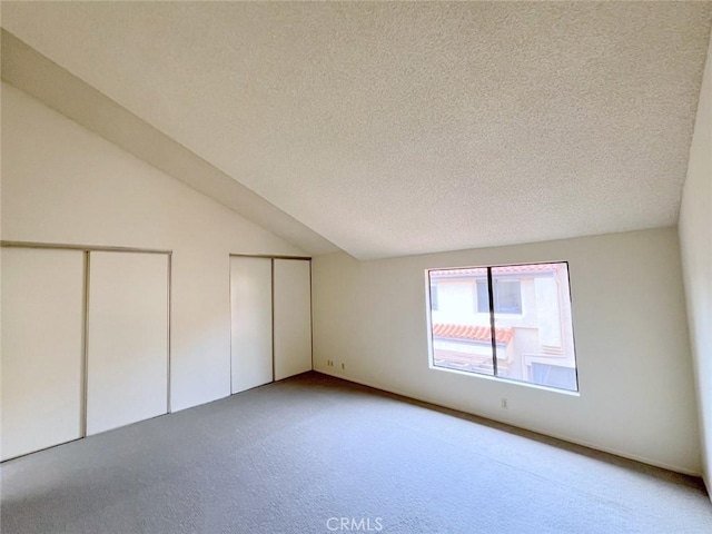 unfurnished bedroom featuring multiple closets, carpet, lofted ceiling, and a textured ceiling