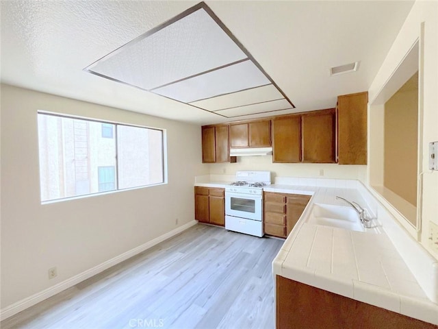 kitchen featuring sink, a textured ceiling, tile counters, white gas range, and light hardwood / wood-style floors