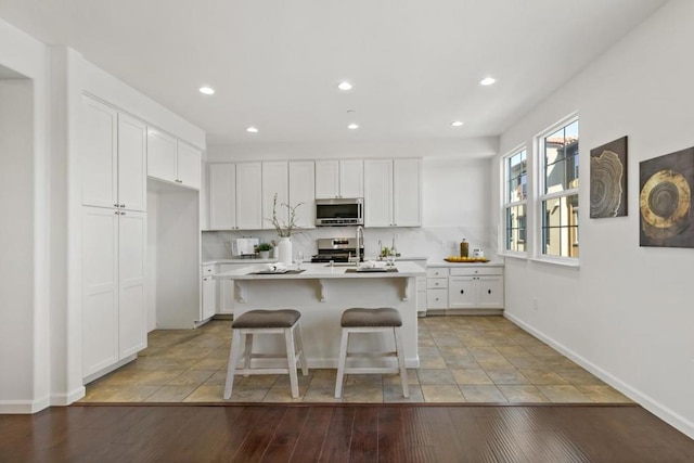 kitchen featuring appliances with stainless steel finishes, a kitchen island with sink, a breakfast bar area, and white cabinets