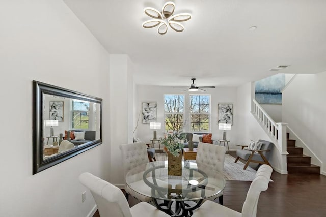 dining space with ceiling fan with notable chandelier and dark hardwood / wood-style flooring