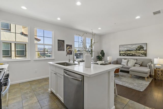 kitchen with sink, stainless steel appliances, an island with sink, white cabinets, and a kitchen bar