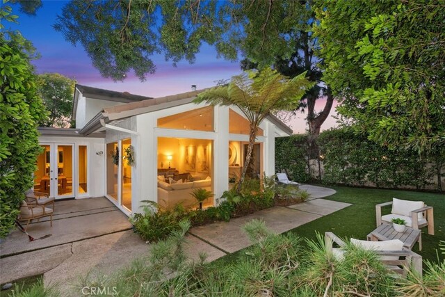 back house at dusk featuring french doors, a patio area, and a lawn